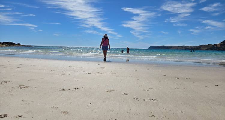 Person, die entlang eines sandigen Strandes spaziert mit Blick auf Klippen in der Ferne.