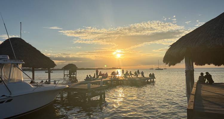 Personas disfrutando de la vista del atardecer desde un muelle en el agua.