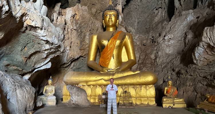 Persoon die staat voor een gigantisch gouden Boeddhabeeld in een grot.