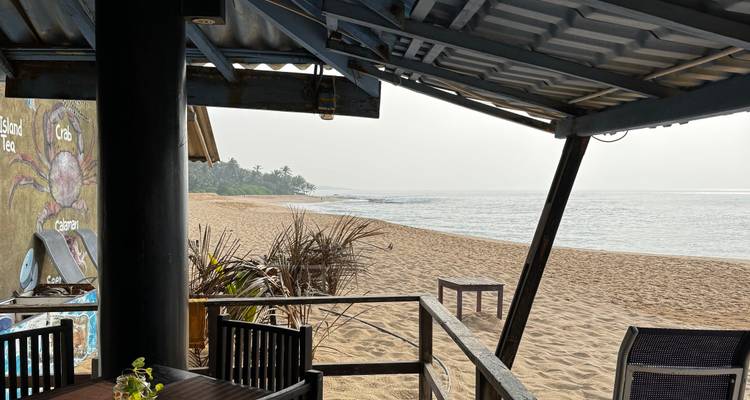 Vue sur la plage depuis sous un toit avec une mer calme et un rivage sablonneux.