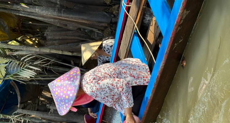 Two people in a boat wearing traditional hats navigating through mangroves.