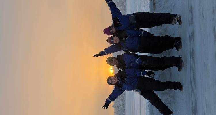 Groep vrienden die genieten van een besneeuwde landschap bij zonsondergang, poserend met opgeheven armen.