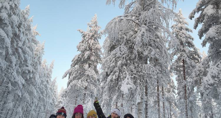 Groep vrienden die poseren in een besneeuwd bos, winterkleding dragend en glimlachend.