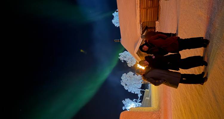 Drie mensen die staan met het noorderlicht en een met sneeuw bedekt landschap op de achtergrond.