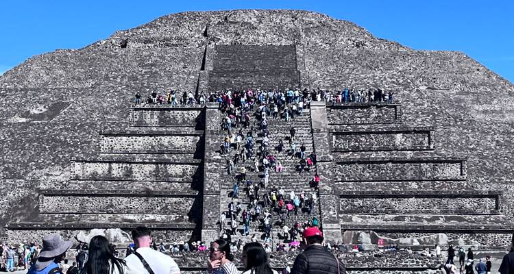 Grote groep mensen die de trappen van een oude piramide beklimt.