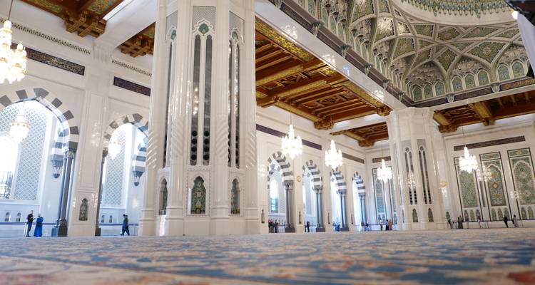 Somptueuse salle de prière de la Grande Mosquée du Sultan Qaboos avec ses colonnes de marbre blanc élancées, ses arcs ornementés et ses lustres étincelants.