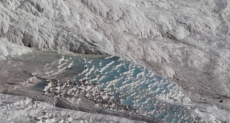 Terrazas de travertino de Pamukkale con reflejo de agua bajo un cielo brillante.