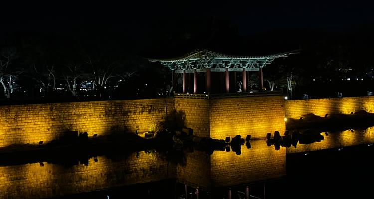 Vue de nuit d'un pavillon coréen traditionnel aux murs illuminés.