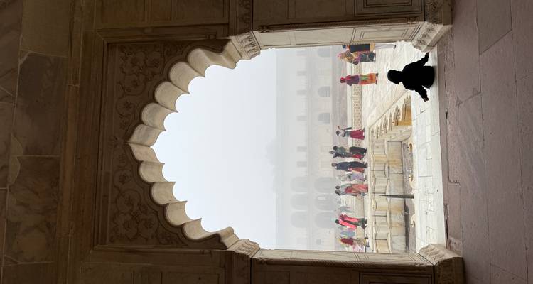 Des touristes à l'intérieur d'un site historique avec des fenêtres en arc et une vue brumeuse à l'extérieur.