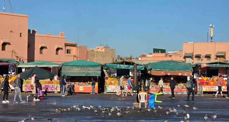 Busy market with people walking and colorful stalls under clear blue sky.