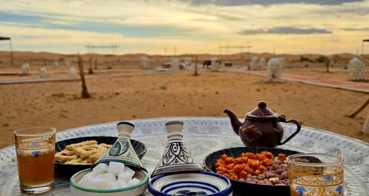 Table with traditional Moroccan tea setup in a desert setting at sunset with tents in the background.