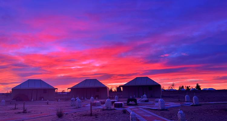 Colorful sunset sky over desert huts, creating a vibrant landscape with scattered tents.
