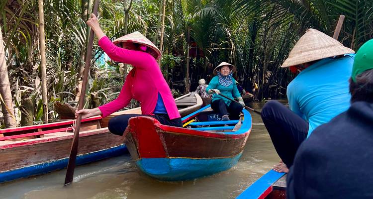 Groep mensen in traditionele boten die door een smalle waterweg navigeren omringd door bomen.