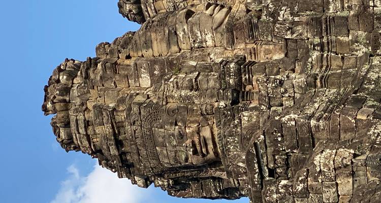Gros plan détaillé des visages géants et sereins en pierre du temple du Bayon sous un ciel bleu.