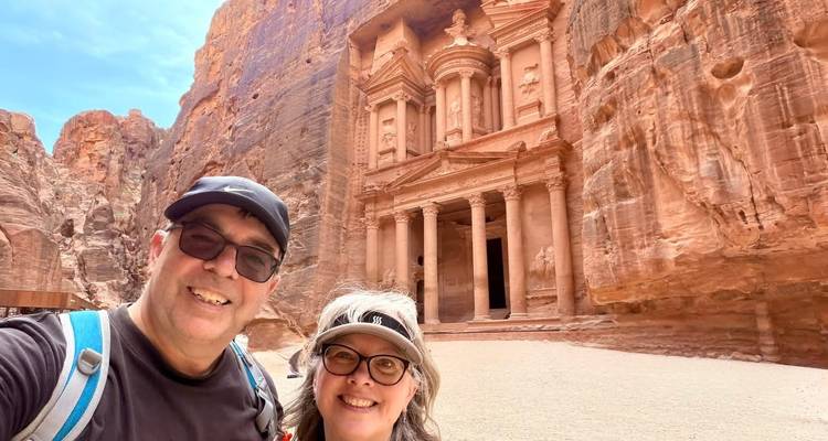 Pareja feliz posando frente al icónico Tesoro de color rosa-rojizo de Petra tallado en el acantilado.