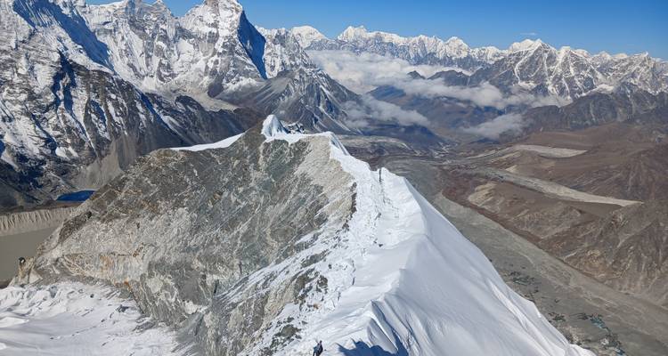Vaste panorama himalayen de crêtes neigeuses déchiquetées contrastant avec des vallées rocheuses sous un ciel cristallin.
