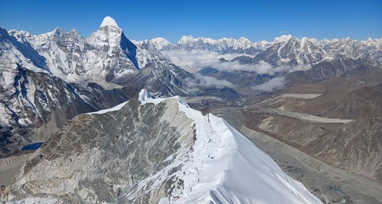 Vaste scène alpine montrant une crête neigeuse en arête de couteau avec l'imposant Ama Dablam et l'Himalaya environnant.