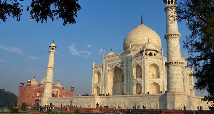 El Taj Mahal de mármol blanco resplandece bajo un cielo azul despejado con visitantes en su base.