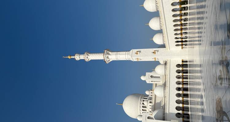 Dômes blancs immaculés et minaret de la Grande Mosquée Sheikh Zayed contre un ciel bleu clair.