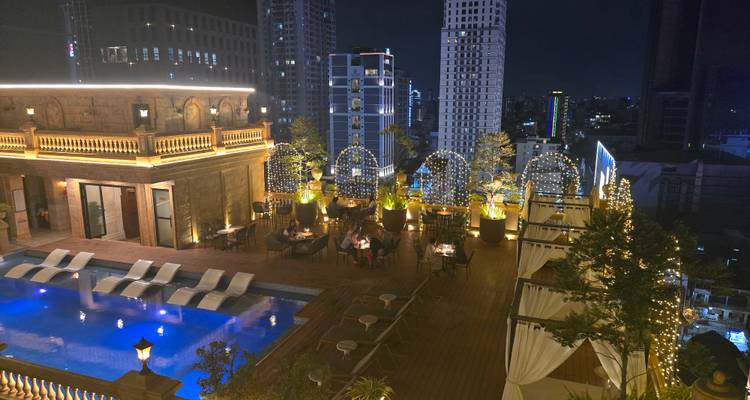 Stijlvol dakterras restaurant en infinity pool 's nachts met uitzicht op een moderne stadshorizon met gasten die dineren onder lichtslinger.