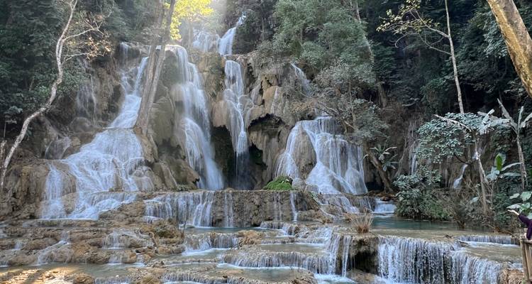 Multi-tiered Kuang Si waterfall cascades through limestone pools surrounded by dense green jungle.