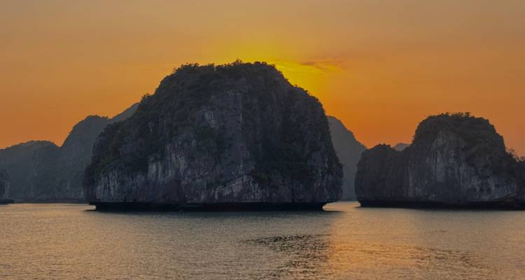Vista de hora dorada de islas kársticas que se elevan desde aguas tranquilas en la Bahía de Ha Long al atardecer.