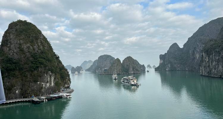 Vista serena de aguas jade y pináculos de piedra caliza imponentes de la Bahía de Ha Long con cruceros navegando.