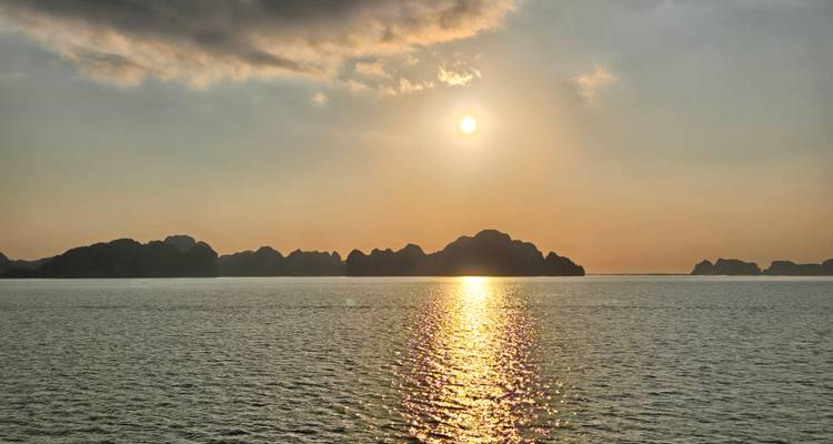 Le soleil se couche sur les îles calcaires de la baie d'Halong projetant un reflet doré sur l'eau calme.