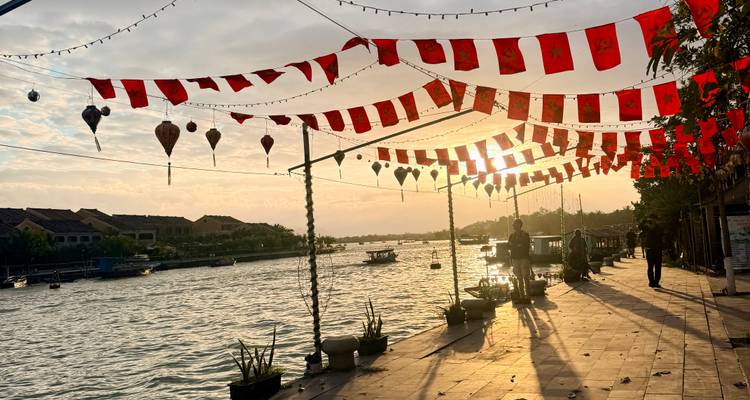 Riverside promenade decorated with red lanterns and flags at sunset, casting long shadows on the pavement.