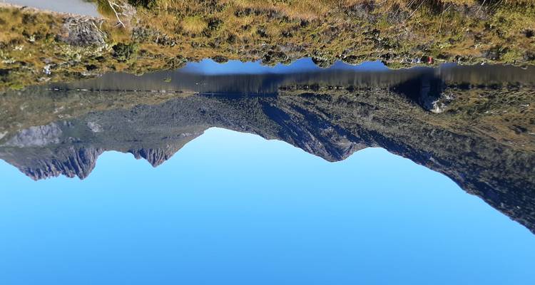 Lac cristallin entouré des pics escarpés de Cradle Mountain sous un ciel bleu éclatant.
