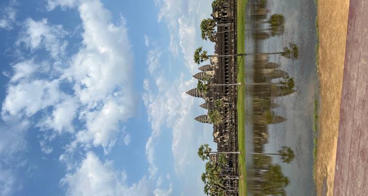 Icónico templo de Angkor Wat reflejado en el foso tranquilo bajo cielos parcialmente nublados.