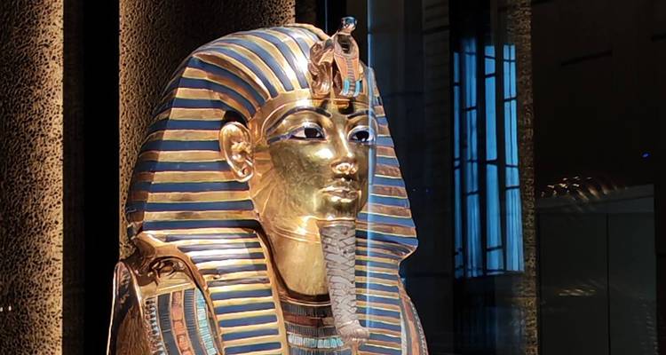 Máscara funeraria de oro y lapislázuli de Tutankamón brilla bajo los focos del museo con reflejos en el cristal.