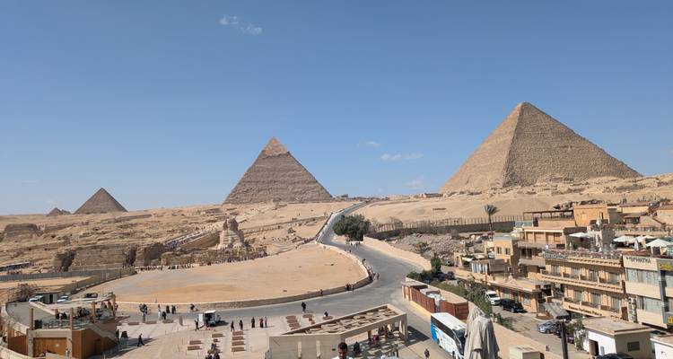 Les emblématiques Grandes Pyramides de Gizeh s'élèvent au-dessus des sables du désert sous un ciel bleu dégagé avec des visiteurs éparpillés en contrebas.