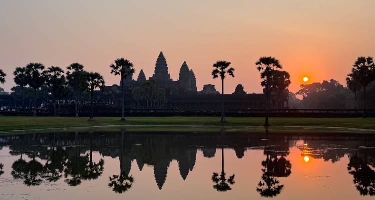Vista icónica del amanecer de Angkor Wat reflejado perfectamente en un estanque tranquilo con palmeras silueteadas.