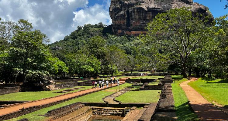 Los visitantes caminan por antiguos jardines paisajísticos bajo la imponente Fortaleza de la Roca Sigiriya.