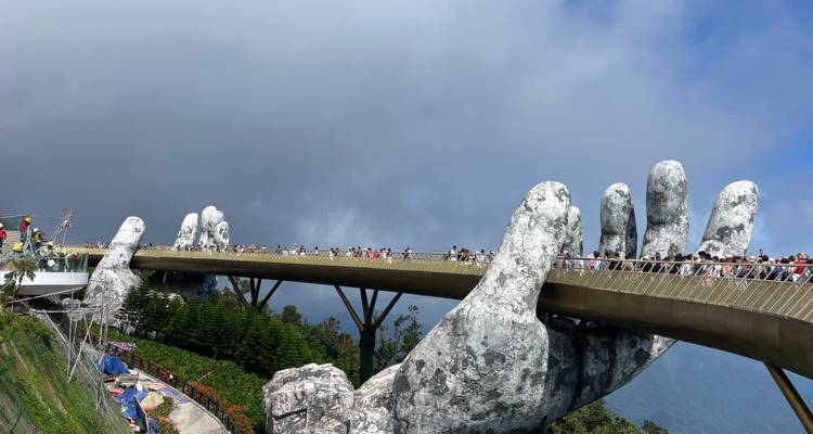 El espectacular Puente Dorado sostenido por manos gigantes de piedra se extiende a través de montañas brumosas mientras los visitantes caminan por él.
