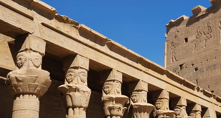 Fila de columnas de arenisca antigua coronadas con capiteles con cabeza de Hathor contra un cielo azul profundo.
