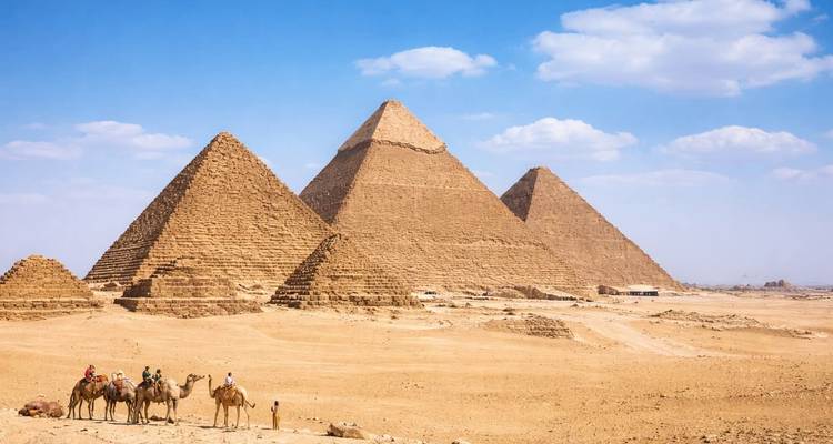 Klassisches Wüstenpanorama der drei Pyramiden mit Kamelreitern, die den Sand durchqueren