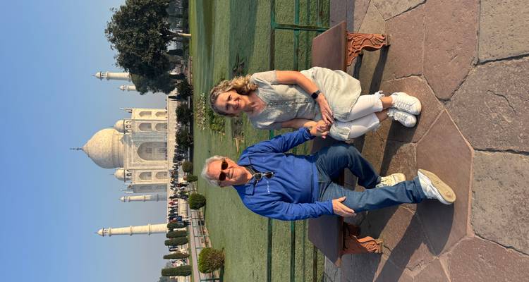 Una pareja se sienta en un banco con el icónico Taj Mahal perfectamente enmarcado en la luz de la mañana detrás de ellos.