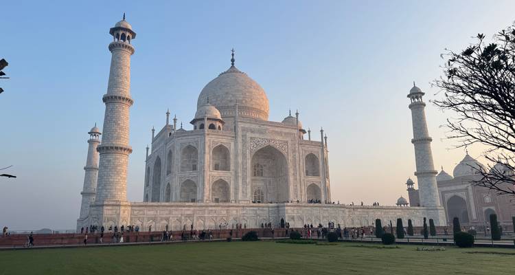 Perspectiva lateral del reluciente Taj Mahal de mármol blanco al amanecer con cielo suave de colores pastel.