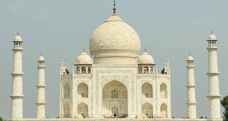Façade de marbre symétrique du Taj Mahal encadrée contre un ciel bleu brumeux.