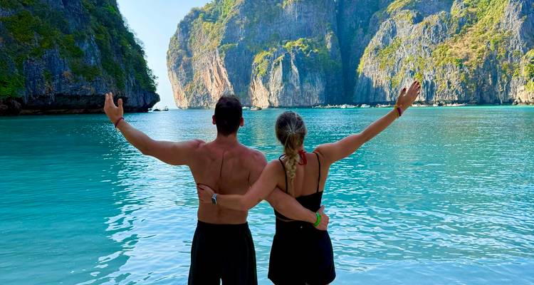 Stel met opgeheven armen gericht naar turquoise Maya Bay en torenhoge kliffen