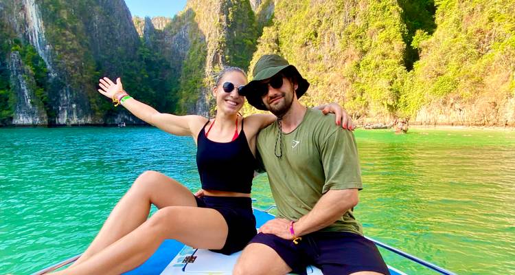 Glimlachend stel zittend op de boeg van een speedboot in turquoise water omringd door kalkstenen kliffen.
