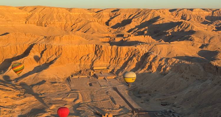 Heteluchtballonnen drijven over de dramatische oranje kloven en grafingangen van de Vallei der Koningen bij zonsopgang