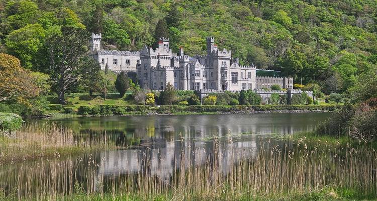 La Abadía de Kylemore reflejada en un lago tranquilo rodeado de un exuberante bosque verde.