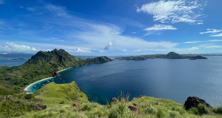 Vue panoramique emblématique depuis l'île de Padar montrant des baies turquoise, des crêtes vertes et une mer bleu profond sous un ciel lumineux.