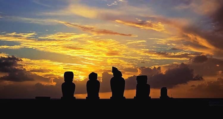 Siluetas de moais contra un cielo dorado dramático del amanecer con nubes estriadas.