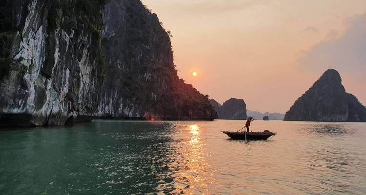 Un rameur solitaire glisse devant d'imposantes falaises calcaires dans la baie d'Halong au coucher du soleil.