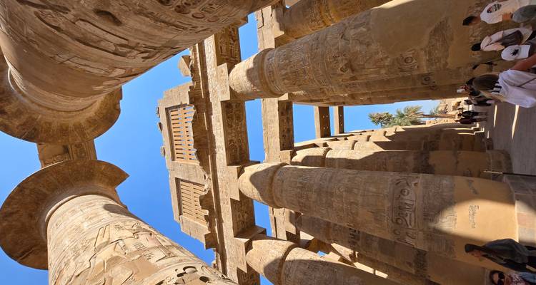 Opwaartse blik door de hypostyle hal van de Karnak Tempel met massieve gebeeldhouwde zandstenen zuilen tegen een blauwe hemel