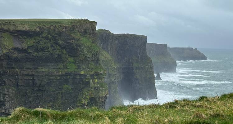 Les falaises abruptes de Moher striées de vert plongent dans les vagues déferlantes de l'Atlantique sous un ciel orageux.